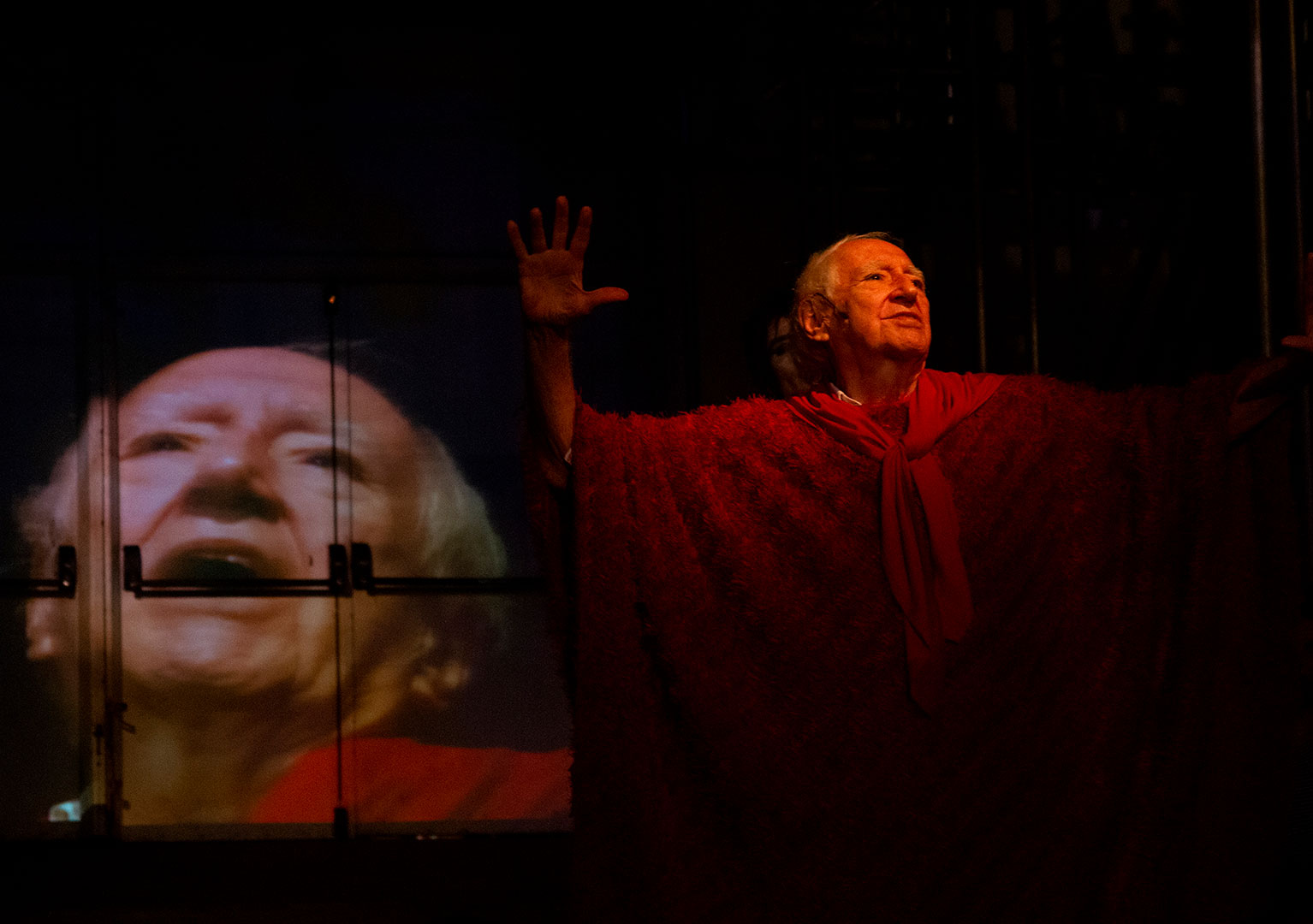 Na foto, o diretor Z&eacute; Celso atuando, atr&aacute;s dele &eacute; poss&iacute;vel ver portas claras onde o rosto dele &eacute; projetado.