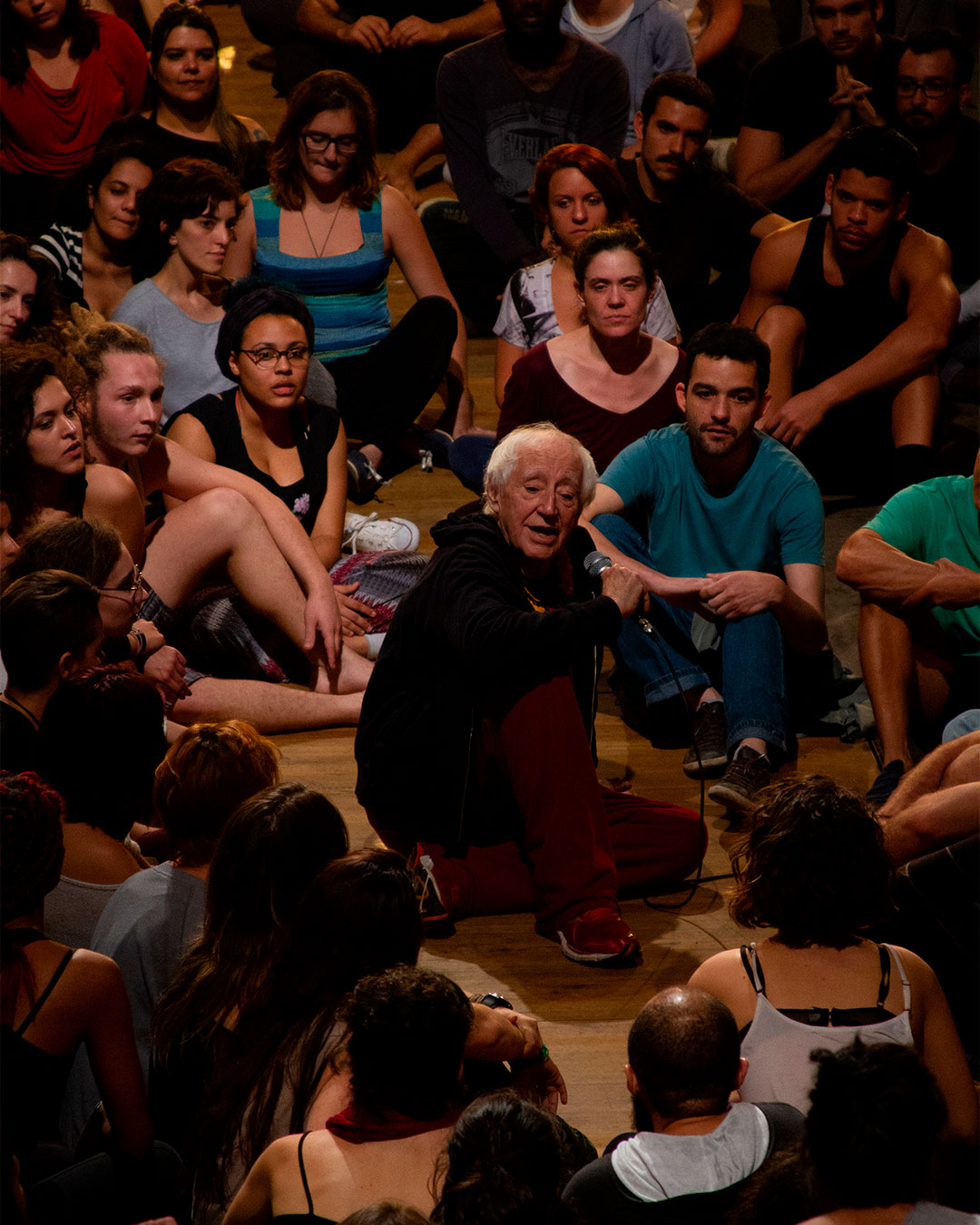 O diretor Z&eacute; Celso falando em um microfone rodeado de pessoas que o escutam.
