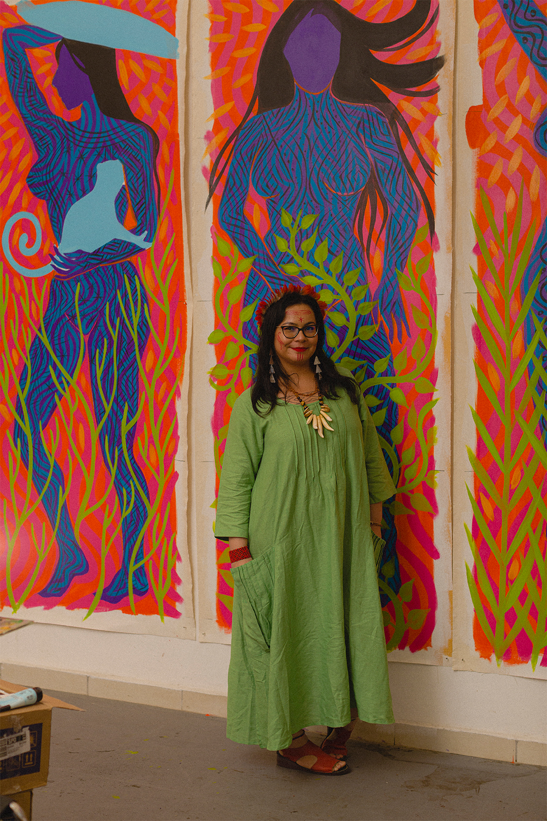 Fotografia de Daiara Tukano ao lado de uma pintura dela.